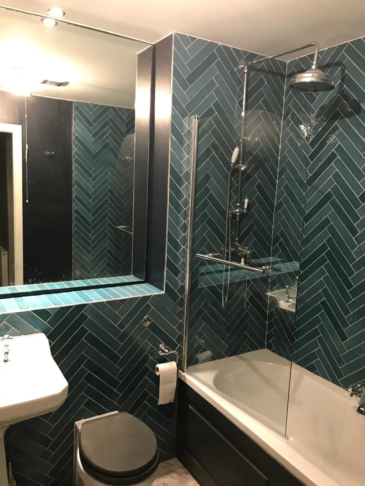 Completed bathroom with green herringbone tiles and a glass shower screen